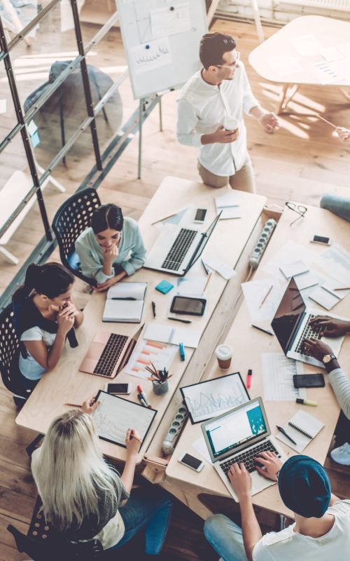 Top view of multiracial young creative people in modern office. Group of young business people are working together with laptop, tablet, smart phone, notebook. Successful hipster team in coworking. Freelancers.